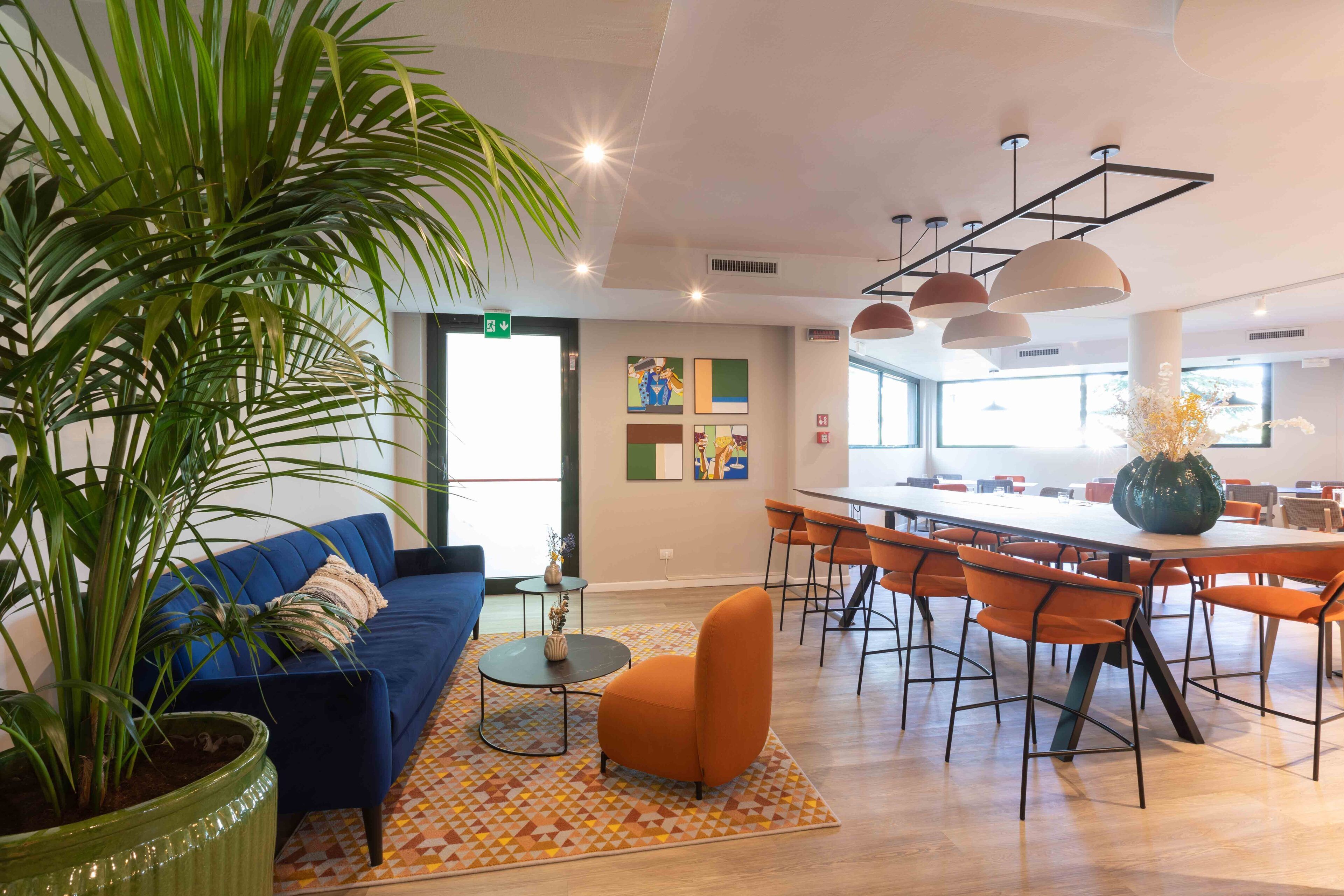 Un espacio moderno para estar con un sofá azul, un sillón naranja y una planta grande en maceta.