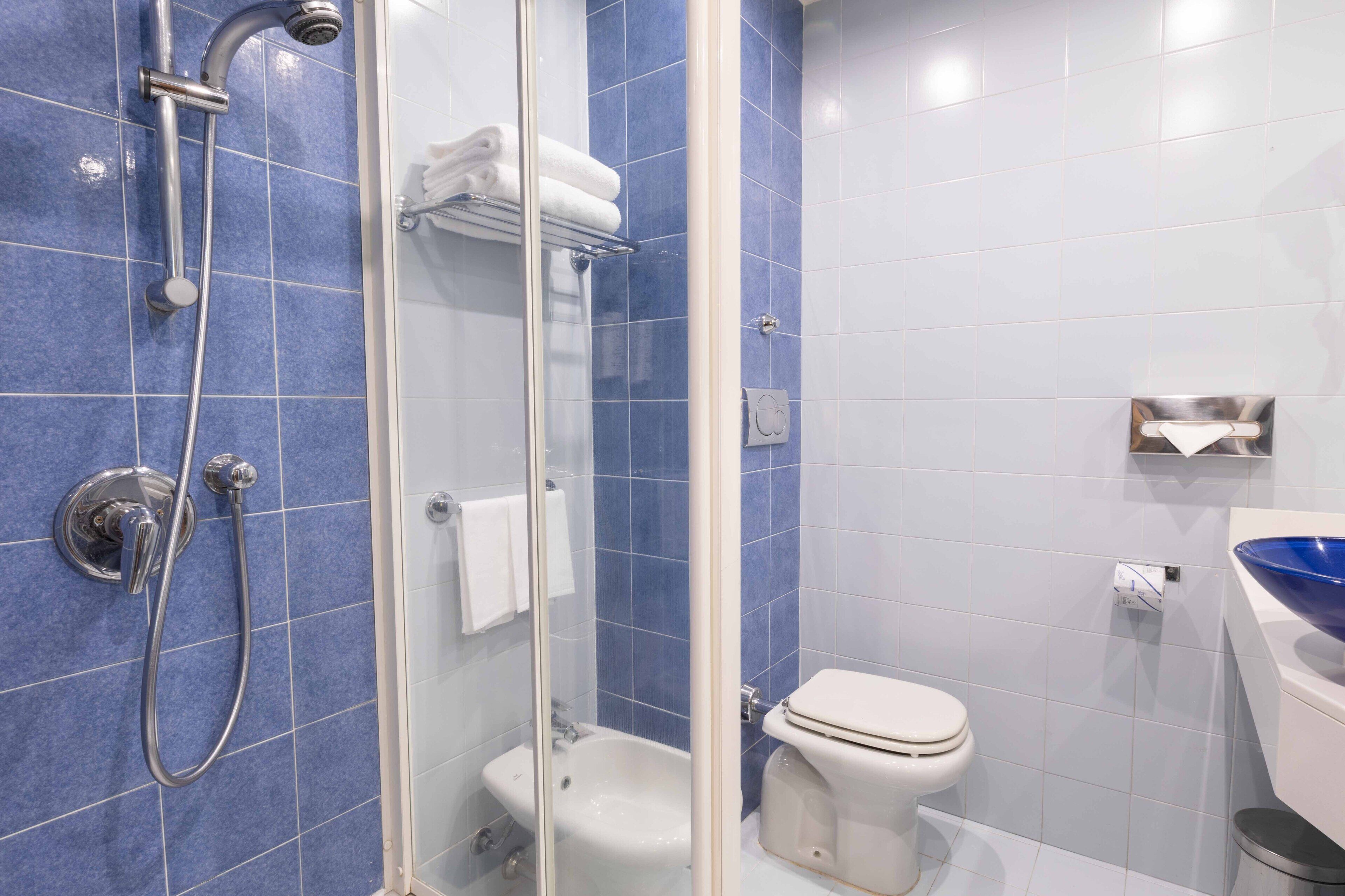 A bathroom with blue tiles, a glass-enclosed shower, a white toilet, and a sink with a blue basin.
