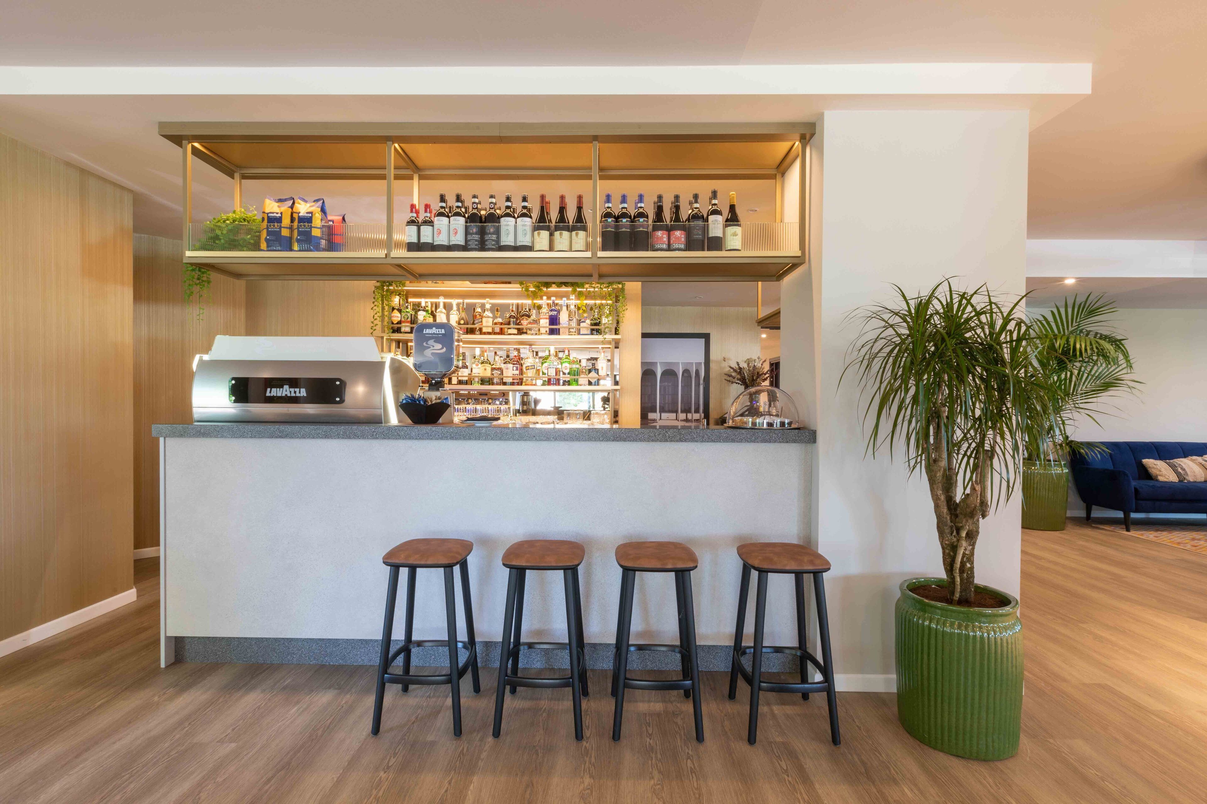A modern kitchen with a bar area, a coffee machine, and a potted plant.