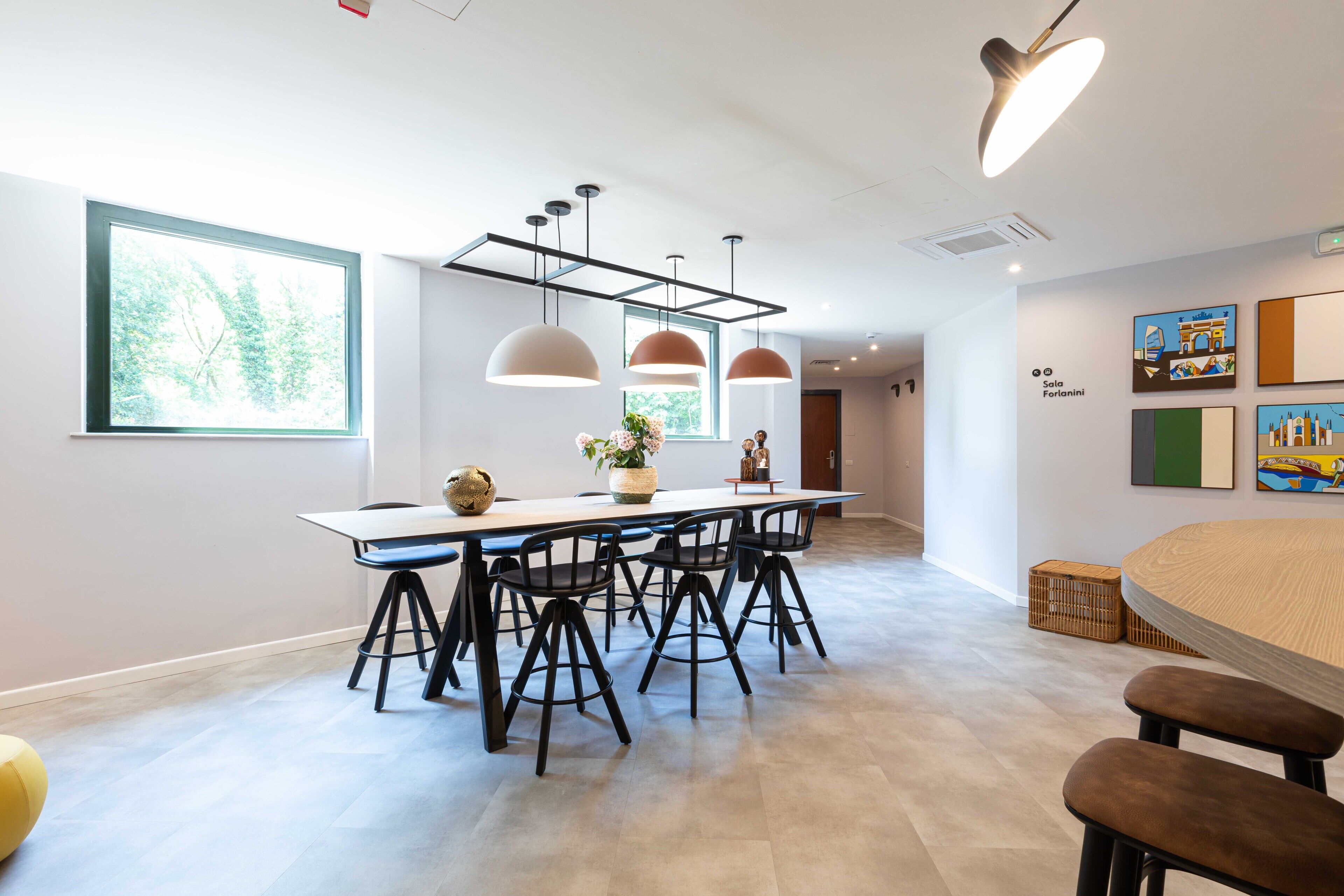 Een moderne eetruimte met een lange tafel, zwarte stoelen, hanglampen en kunst aan de muren.