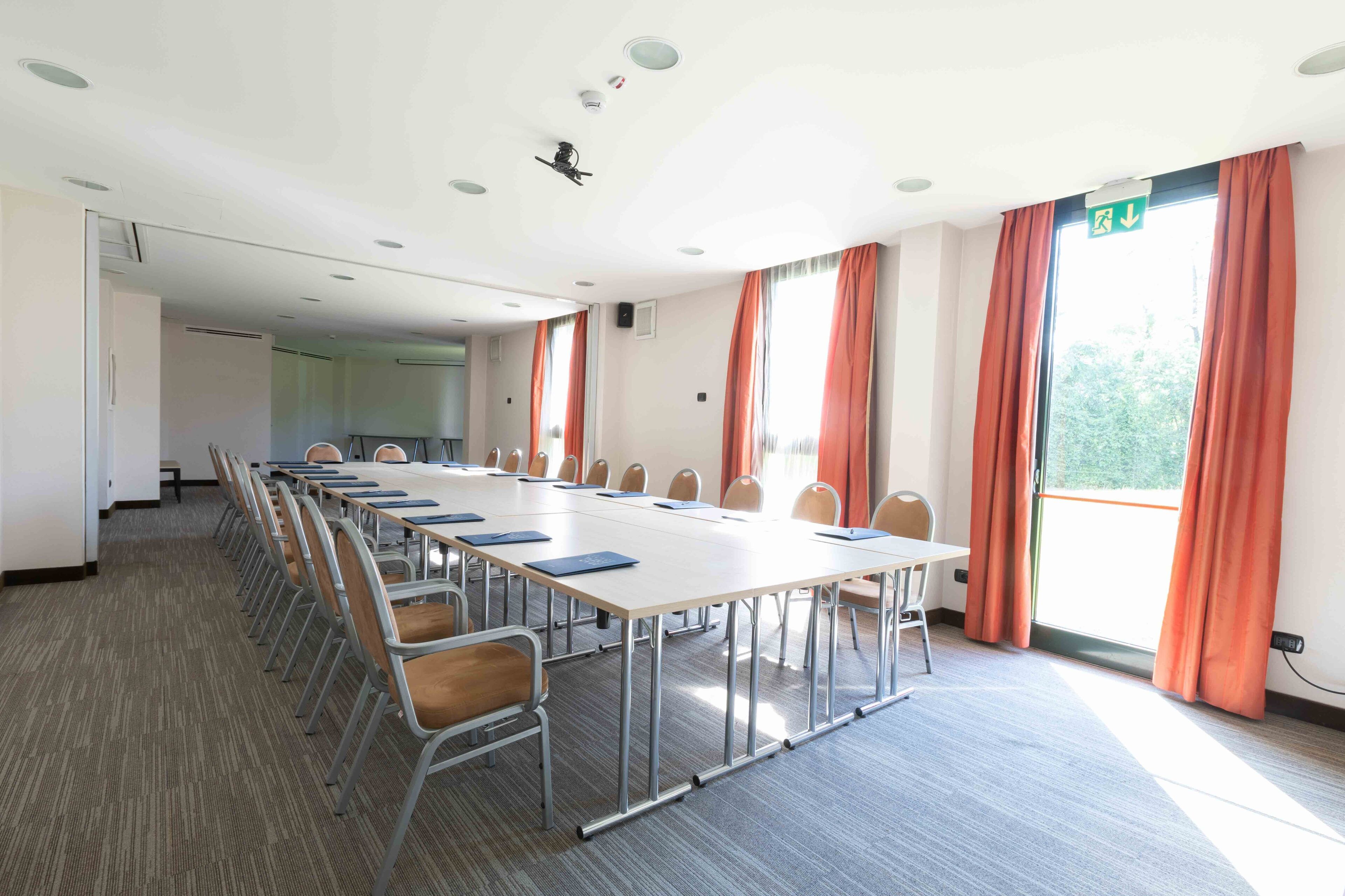 Une salle de conférence avec une longue table, des chaises et une grande fenêtre avec des rideaux.