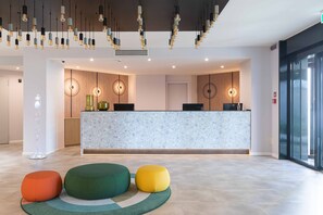 Una zona de recepción moderna con mostrador de mármol, iluminación colgante y asientos coloridos.