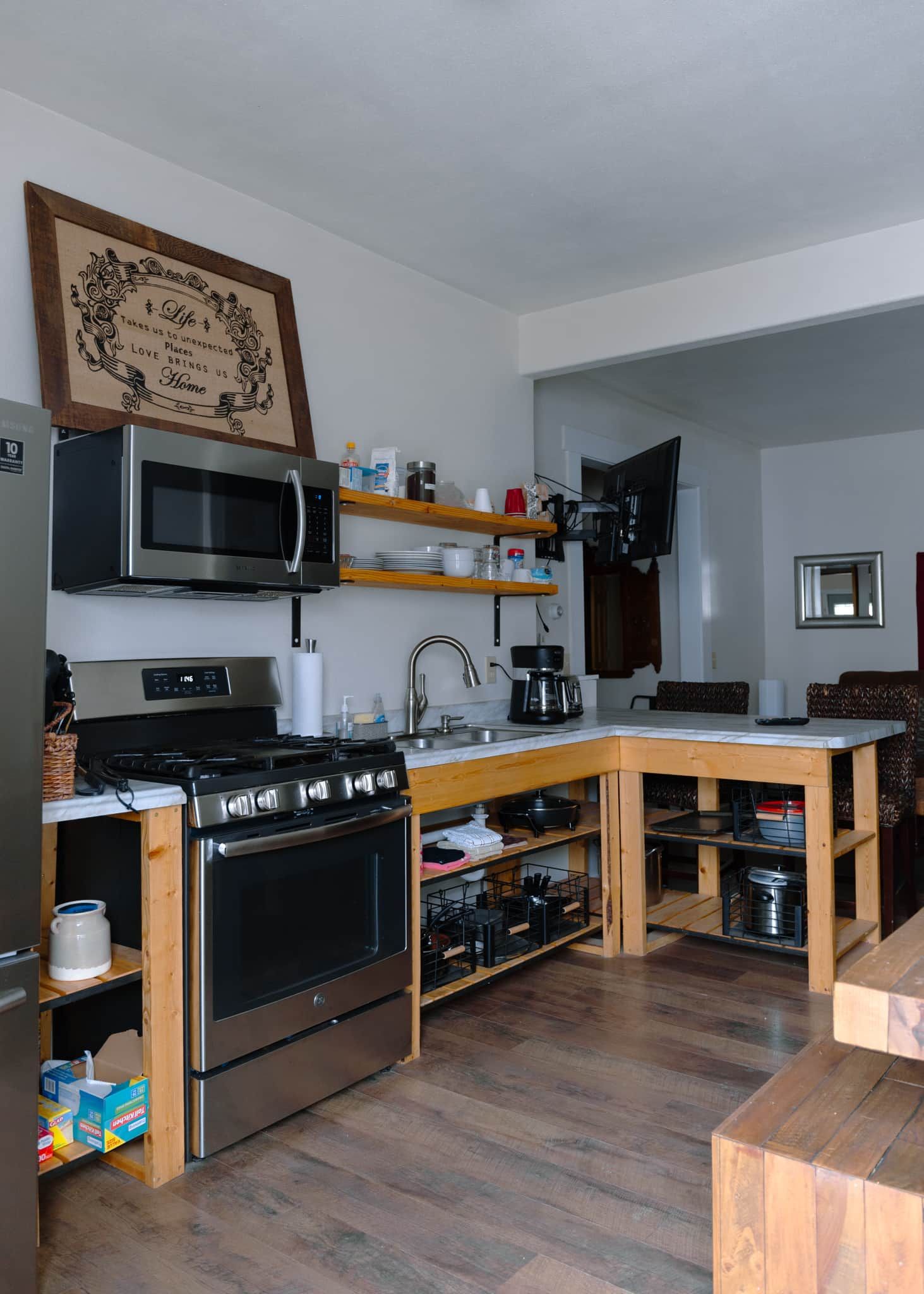 A compact kitchen with a microwave, stove, and wooden shelves.