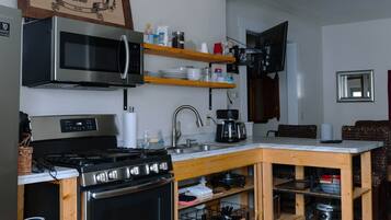 A compact kitchen with a microwave, stove, and wooden shelves.