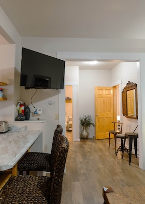 Une pièce dotée d’un téléviseur à écran plat fixé au mur, d’une porte en bois, d’un miroir et d’un coin repas avec une table et des chaises.