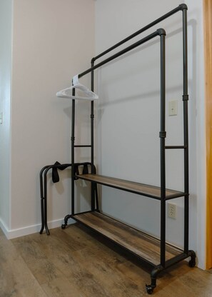 A metal shelf unit with a single shelf and a hanging garment rack against a wall. - East Lodge – Spacious 3BR Stay in Mobridge (Mobridge)