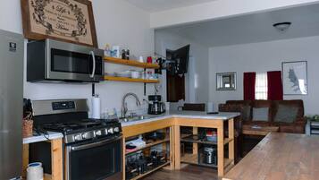 A compact kitchen with a microwave, stove, and wooden table, adjacent to a living area with a sofa and a flat-screen TV.