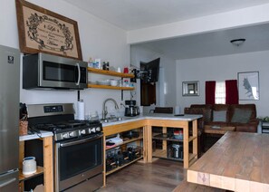 Une cuisine compacte équipée d’un four à micro-ondes, d’une cuisinière et d’une table en bois, jouxtant un espace de vie avec un canapé et un téléviseur à écran plat.