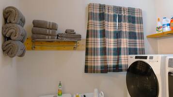 A laundry area with a washing machine, a toilet, and a shelf with folded towels.