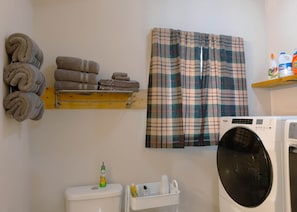 Een wasruimte met een wasmachine, toilet en een plank met opgevouwen handdoeken.