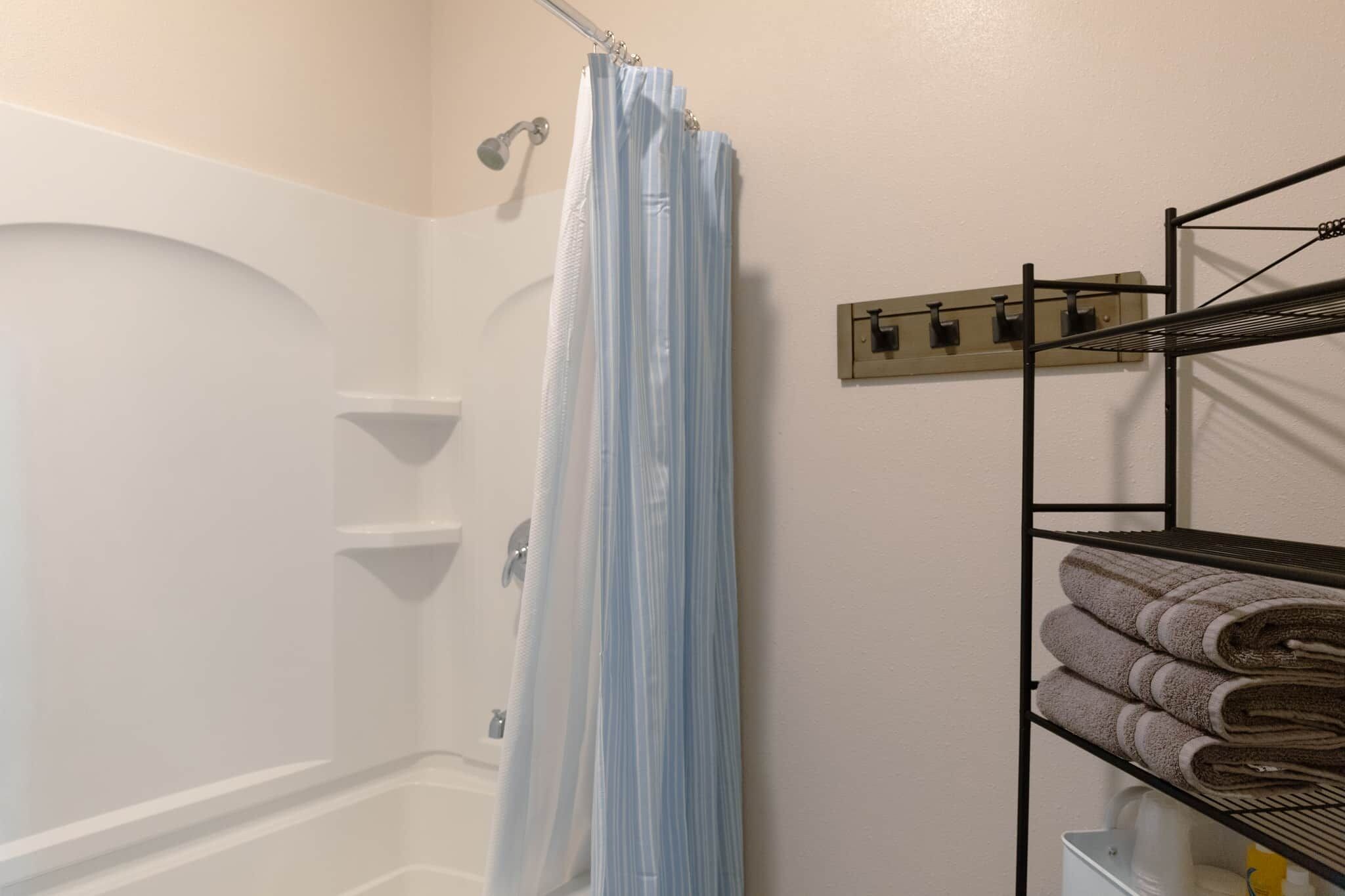 A bathroom with a shower curtain, a towel rack with towels, and a wall-mounted towel rack.