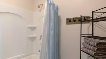 A bathroom with a shower curtain, a towel rack with towels, and a wall-mounted towel rack.