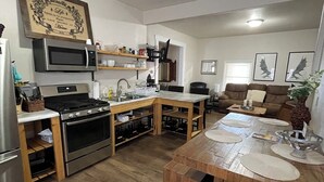 Cocina compacta con horno integrado, microondas y lavamanos. Hay una mesa de comedor con sillas y un pequeño rincón de estar con un sofá.
