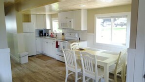 Una cocina compacta con armarios blancos, microondas, estufa y una mesa de comedor con sillas.
