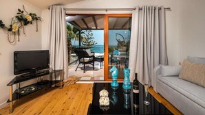Un salon équipé d’un téléviseur, d’un canapé, d’une table basse agrémentée d’objets décoratifs et offrant une vue sur la mer grâce à une porte vitrée.