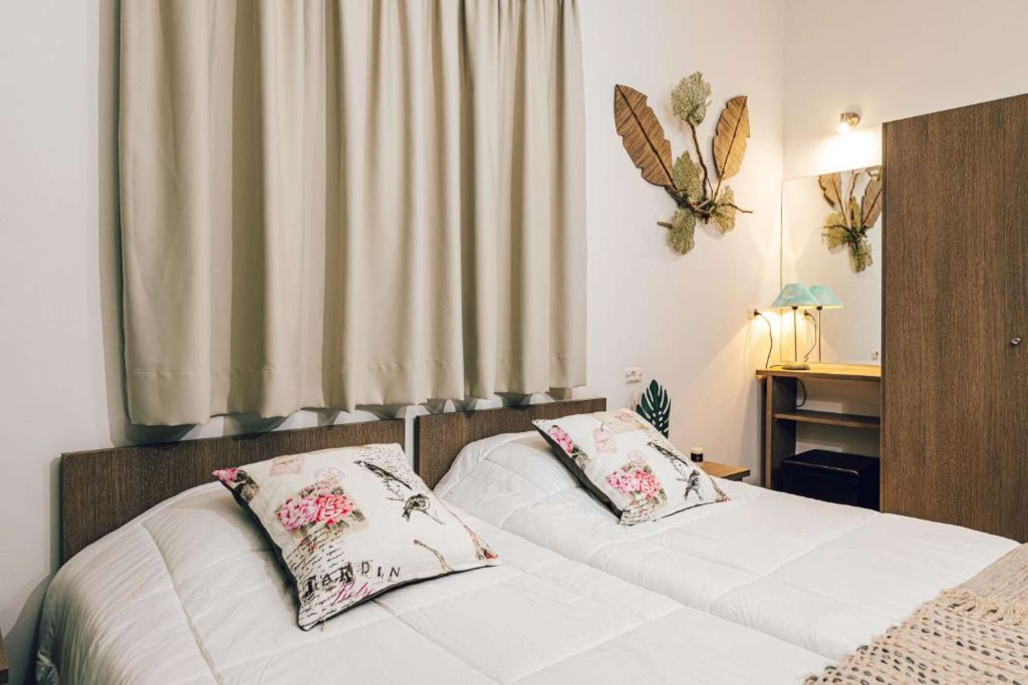 Un lit avec deux oreillers, une table de chevet avec une lampe, un miroir et une armoire.