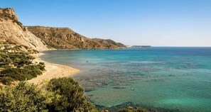 A coastal landscape with a beach, clear waters, and a mountainous backdrop.