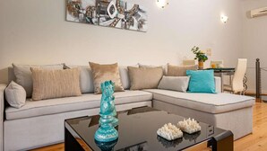 Een moderne woonkamer met een hoekbank, een glazen salontafel en een decoratieve sculptuur.