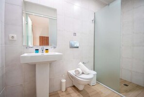 Et badeværelse med en hvid vask, toilet og en brusekabine i glas samt et spejl.