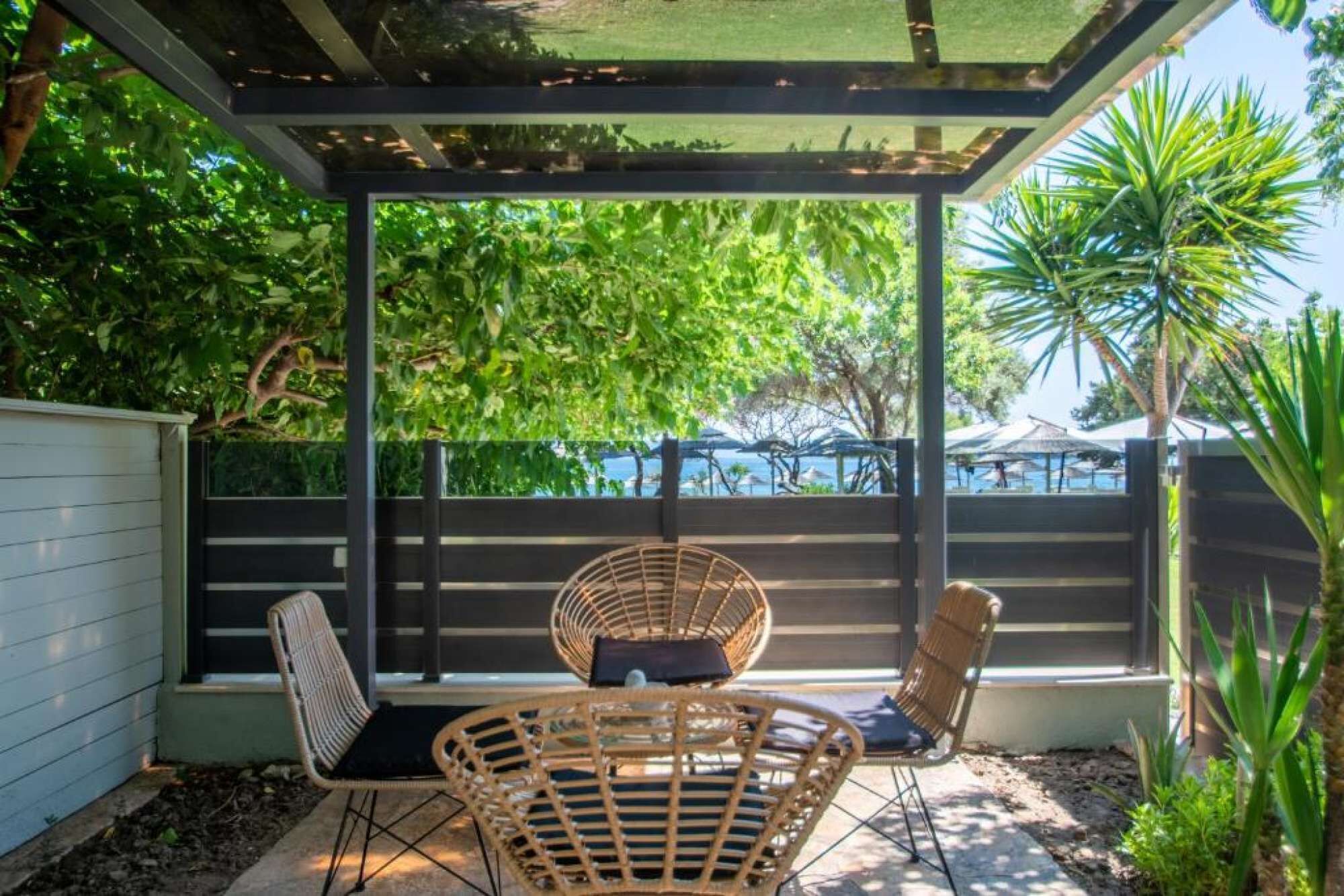 A covered patio with two wicker chairs and a small table, overlooking a pool area with umbrellas.