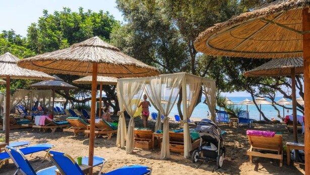 A beach with thatched umbrellas, sun loungers, and a covered seating area. - pelouzo island view II (Vasilikos)