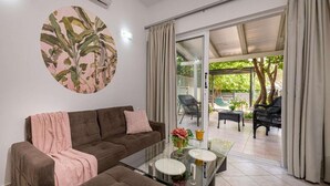 A living room with a sofa, a glass coffee table, and a sliding glass door leading to an outdoor seating area. - pelouzo island view II (Vasilikos)