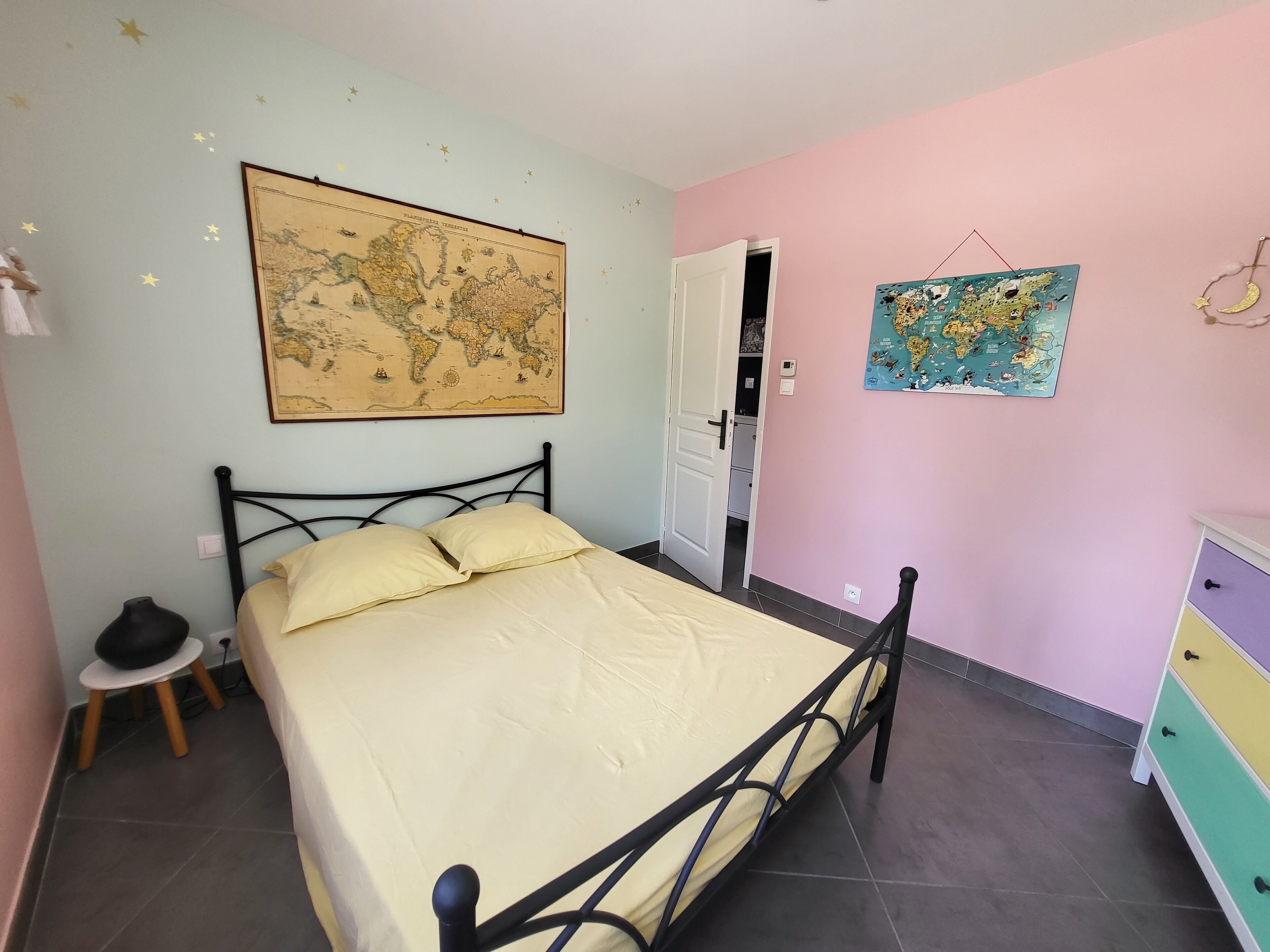 Une chambre à coucher avec un lit, une carte accrochée au mur, une commode et une porte donnant sur une autre pièce.