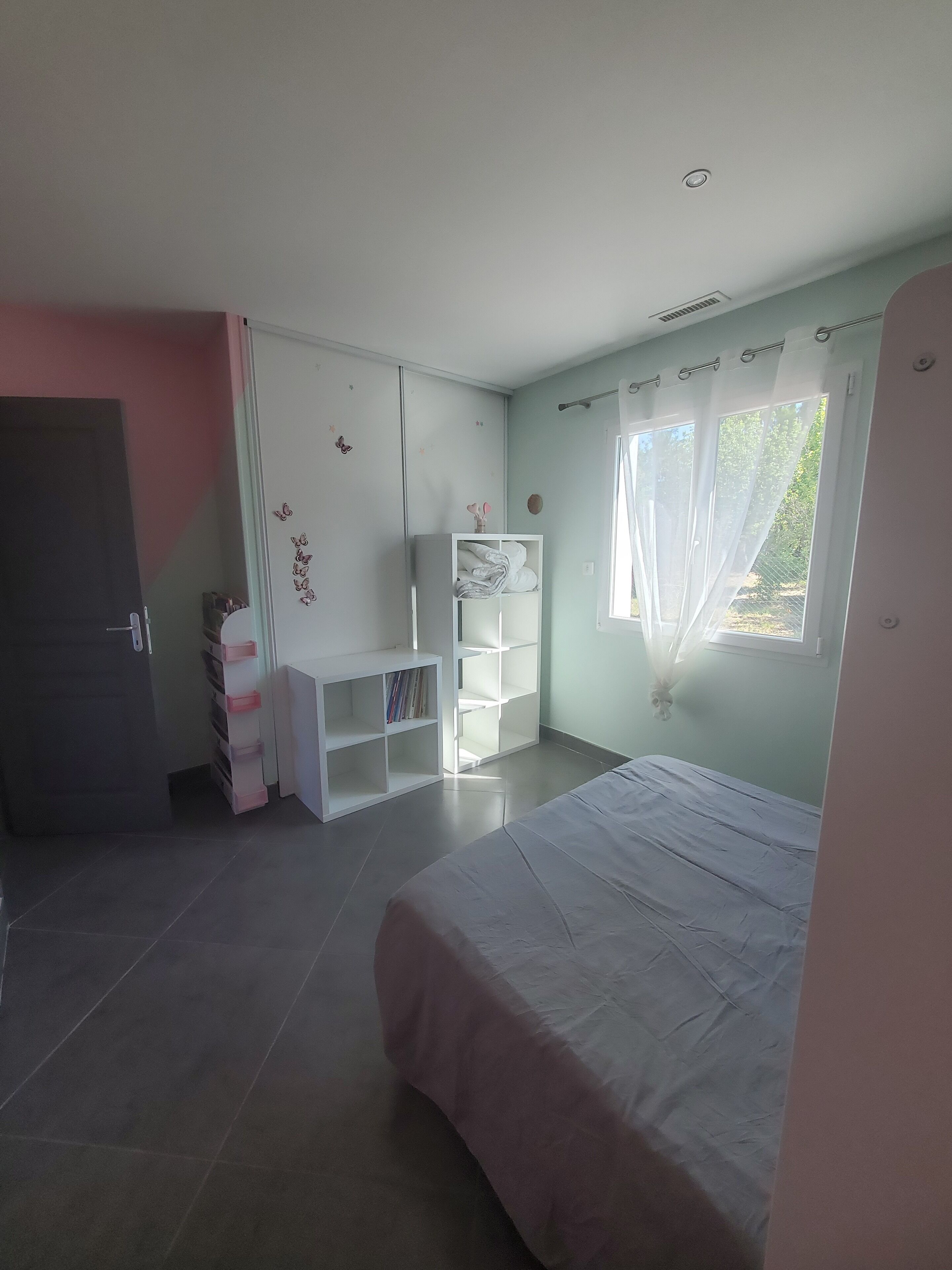 A bedroom with a bed, a wardrobe, a desk, and a window with curtains.