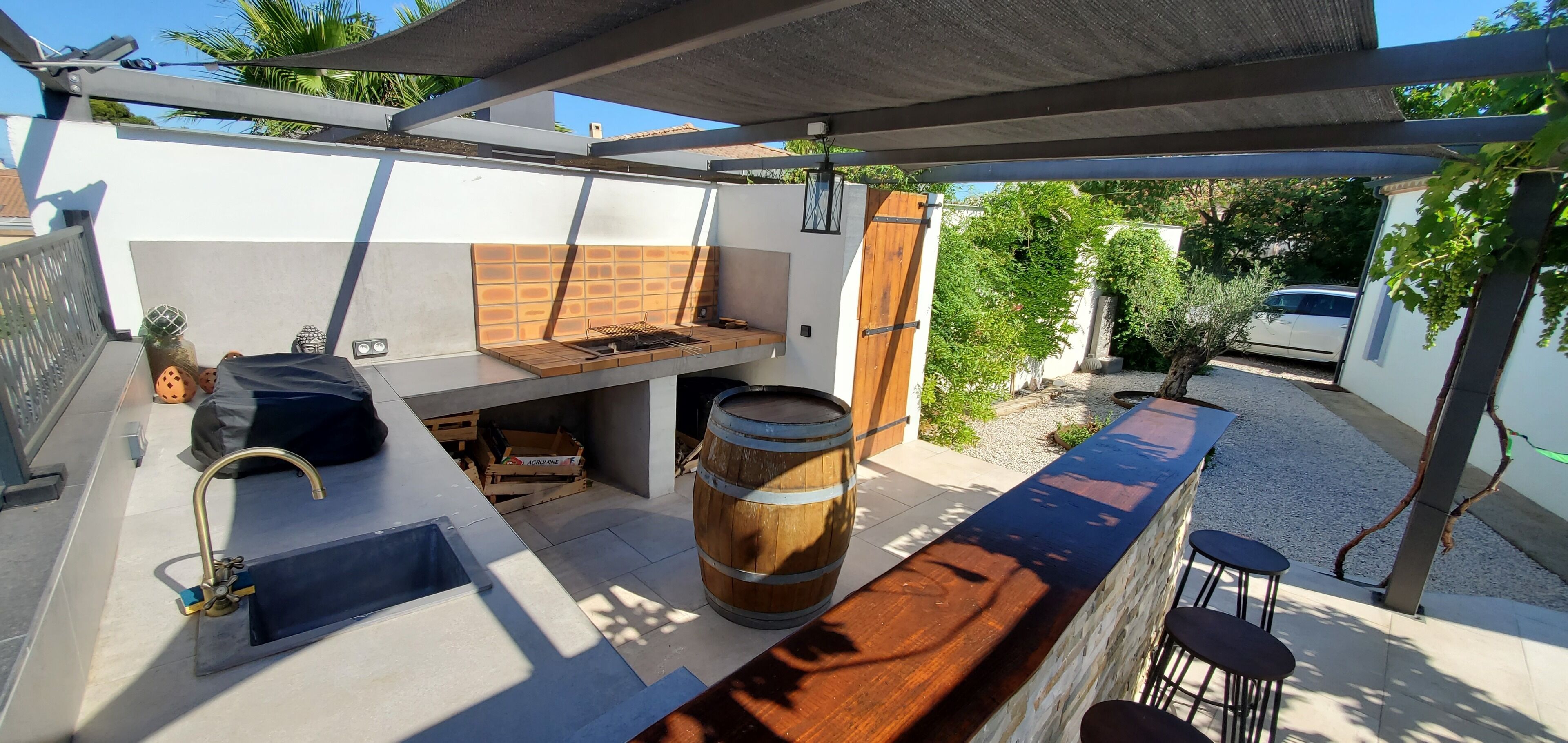 Una cocina al aire libre con una parrilla, un barril de madera y una barra con taburetes.