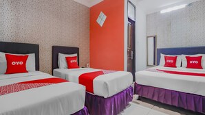 Habitación de hotel con tres camas, cada una con ropa de cama blanca y almohadas rojas. La habitación tiene papel tapiz estampado, una pared de acento roja y un espejo grande.