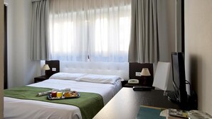 Una camera d'hotel con un letto grande, una scrivania con un computer, una televisione e un vassoio per la colazione sul letto.
