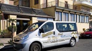 Un autobus navetta bianco parcheggiato di fronte a un edificio con balconi e una palma.