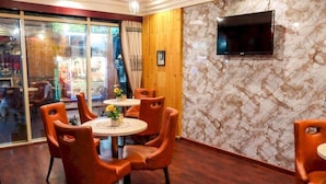 A dining area with a round table, orange chairs, and a TV mounted on a marble wall. - Phoenix Hotel Deira (Dubai)