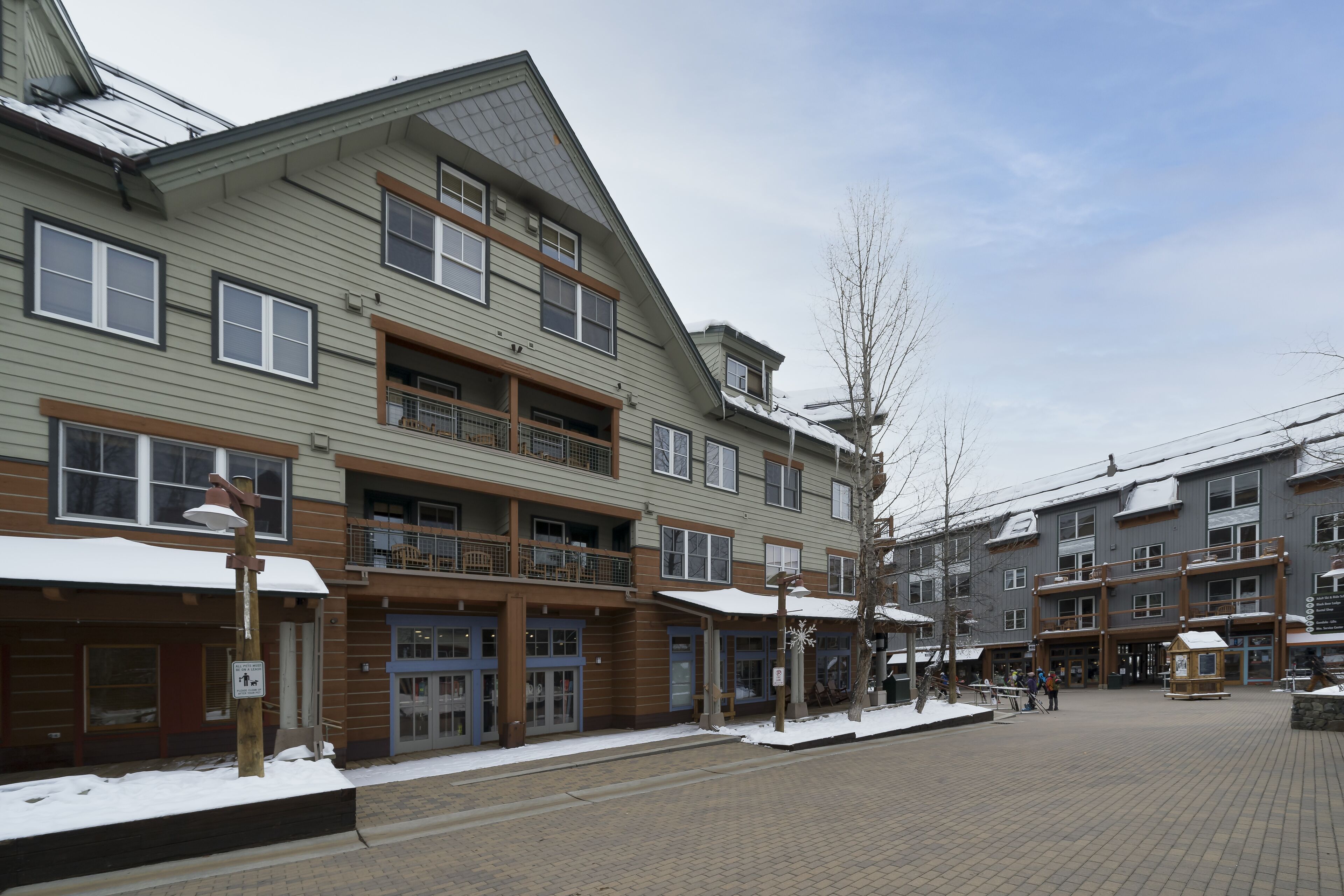 Un immeuble à plusieurs étages, avec une entrée au rez-de-chaussée, des balcons et un sol recouvert de neige.