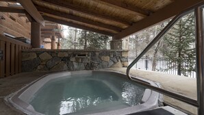 Un bain à remous dot é d’un mur en pierre et de poutres en bois, entouré d’une terrasse en bois et d’un chemin en pierre.