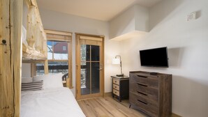 Une chambre à coucher comprenant un lit, une commode en bois, un bureau avec une lampe, un téléviseur et une porte-fenêtre coulissante donnant sur un balcon.