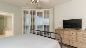 A bedroom with a bed, a TV on a wooden dresser, and a sliding glass door leading to a balcony. - Breathtaking Panoramic Views of the Gulf (Pensacola)