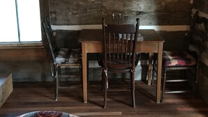 A rustic room with a wooden table and chairs, a window, and a log wall. - 1830’s Log Cabin (Franklinton)