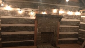 A log cabin interior with a fireplace, wooden walls, and string lights. - 1830’s Log Cabin (Franklinton)