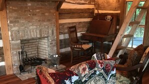 A cozy room with a fireplace, wooden furniture, and a colorful throw blanket on a pink chair. - 1830’s Log Cabin (Franklinton)