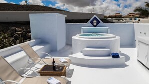 Ein Poolbereich auf dem Dach mit Liegestühlen, einer Whirlwanne und einem kleinen Tisch mit Flasche und Glas.