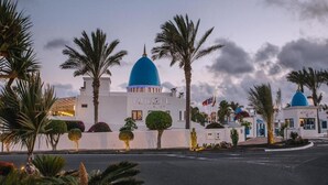 Ein Hotel mit weißen Wänden und blauen Kuppeldächern, Palmen und Flaggen.