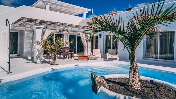 Ein modernes, weißes Gebäude mit Pool, Sitzgelegenheiten im Freien und einer Pergola.