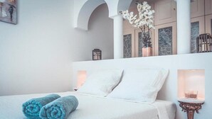 Ein Hotelzimmer mit einem Bett, weißen Leinentüchern, zwei gerollten Handtüchern, einem Nachttisch mit Kerze und einer Wandleuchte.
