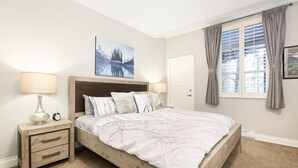 A bedroom with a wooden bed, two bedside tables, a nightstand, a painting, a window with curtains, and a door. - Sprawling Corner Condo, Amazing 1st floor deck, Ski in/out, Sleeps 4 (Whistler)
