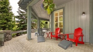 A covered patio with red Adirondack chairs, a stone wall, and a hanging flower basket. - Sprawling Corner Condo, Amazing 1st floor deck, Ski in/out, Sleeps 4 (Whistler)