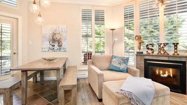 A cozy living room with a fireplace, a dining table, and a sofa with a throw blanket. - Sprawling Corner Condo, Amazing 1st floor deck, Ski in/out, Sleeps 4 (Whistler)