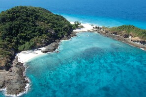 An aerial view of a coastal area with a beach, clear turquoise waters, and dense green vegetation on a hill. - Constance Tsarabanjina Madagascar (Tsarabanjina)