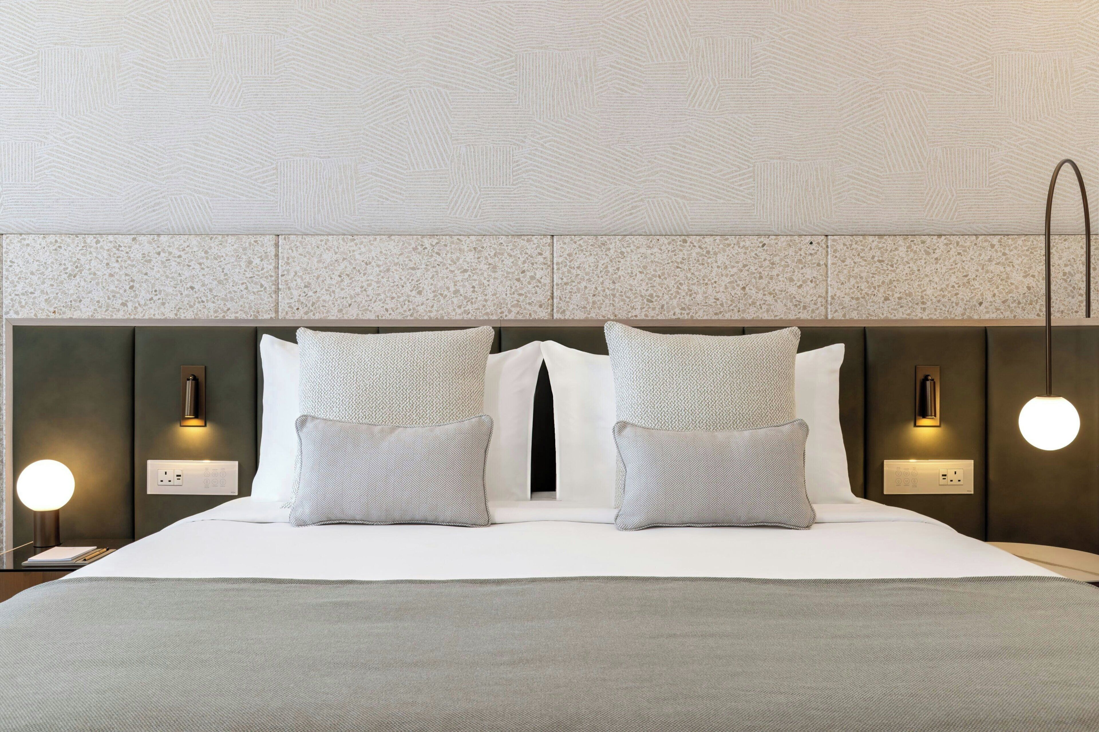 A modern hotel room with a large bed, two bedside lamps, and a headboard with a textured pattern.