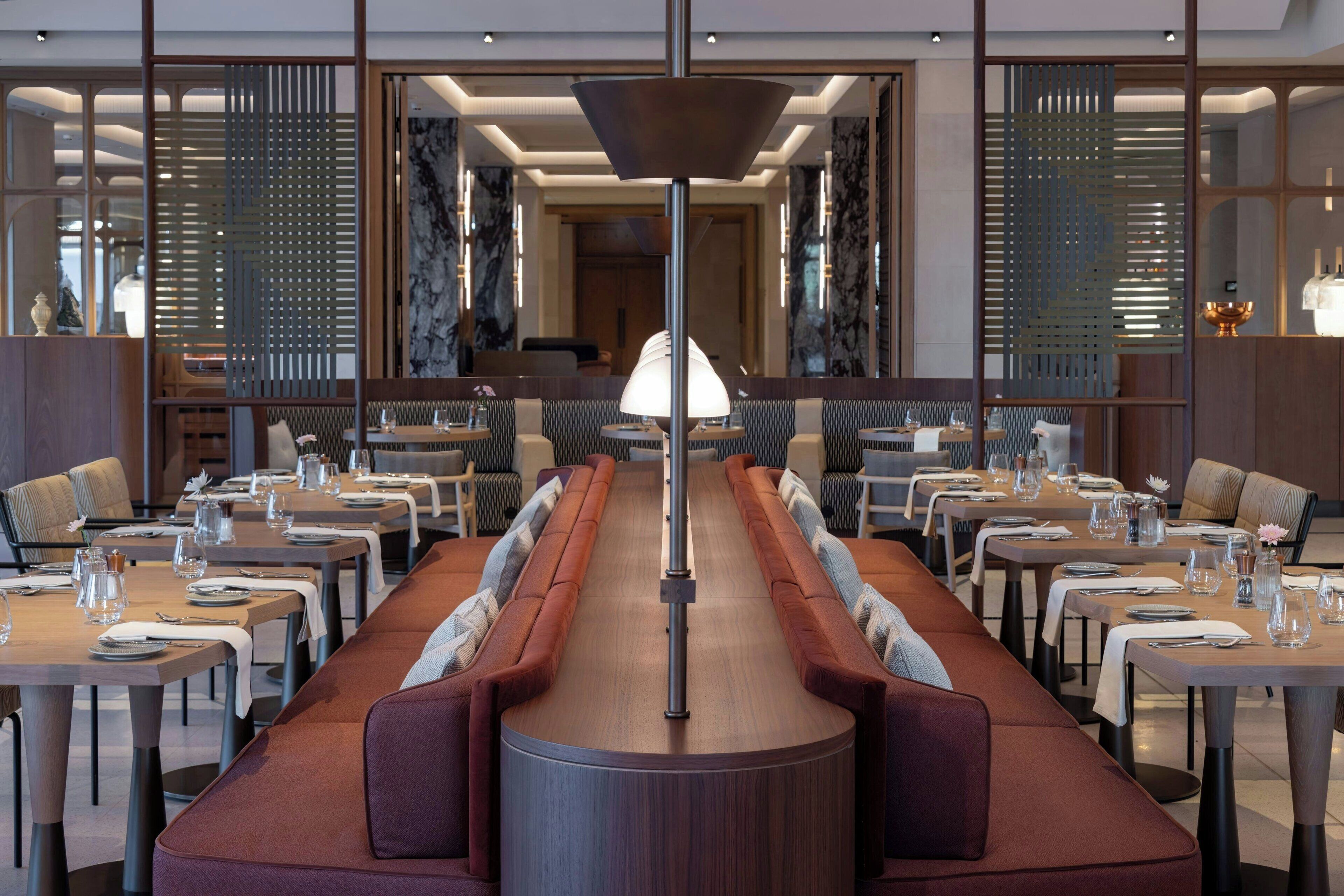 A modern dining area with long tables, cushioned seating, and a central light fixture.